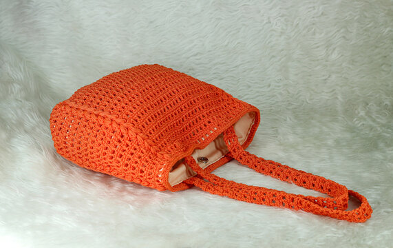 Crocheted handmade orange bag on furry white blanket.