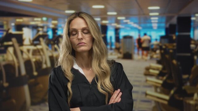 Woman with arms crossed in gym looks irritated, while young blonde judge wearing uniform stands by gymnasium wall indoors.