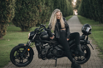 Confident woman in black leather outfit sitting on a stylish black motorcycle outdoors, enjoying...