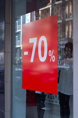 Vertical photo. Red sticker with text 70% on glass showcase window of clothing store. Concept of online shopping, mega discount, 11 november, Black Friday sale, holiday, cyber monday, gift, offer