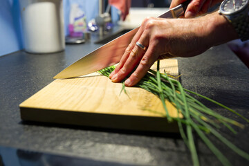 Preparing food at own kitchen with man cutting chive on wooden cutting board on an autumn evening. Photo taken October 6th, 2025, Zurich, Switzerland.