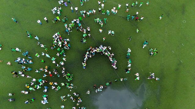 Port Harcourt, Nigeria - 01 October 2025: Aerial view of a vibrant green field dotted with people in white and green, clustered in patterns and arch shapes.