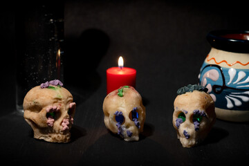 Sugar skulls, a burning candle, and traditional items on a dark day of the dead altar