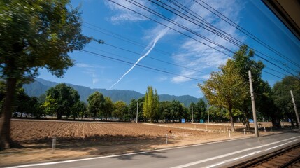 Bright blue skies stretch over a lush landscape as a train travels past fields and trees, highlighting natural beauty and distance