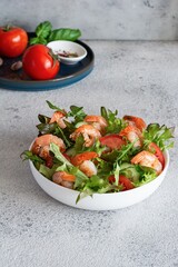 Fresh crispy salad with vegetables and shrimps in a white plate on a light background. Healthy food concept.