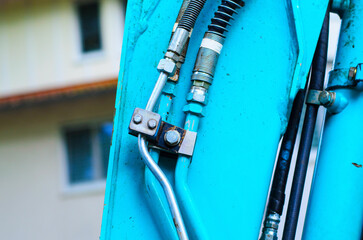 Close up of bright blue excavator arm with hydraulic pipes, hoses, and bolted metal parts