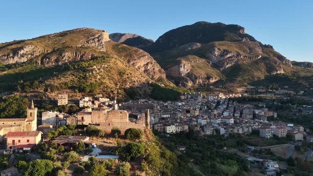 Aerial drone view of Collesano Sicilian mountain town at sunset with Basilica San Pietro church and historic stone streets in the Madonie Mountains, Sicily, Italy. Old mountain town in Sicily