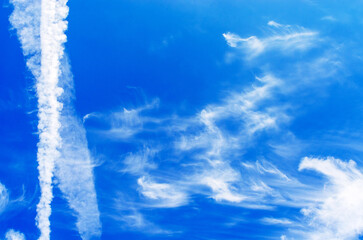 Vibrant blue summer sky with wispy cirrus clouds and a white contrail