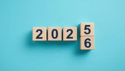 Wooden cubes with changing numbers from 2025 to 2026 on blue background, new year transition and future concept