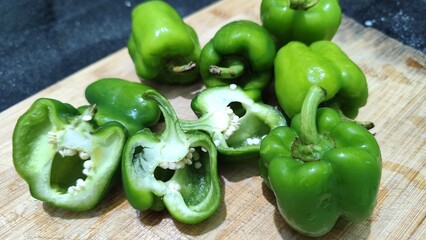 Closeup image of fresh green bell peppers or capsicum placed on a wooden cutting board, with some peppers cut open showing seeds with selective focus.