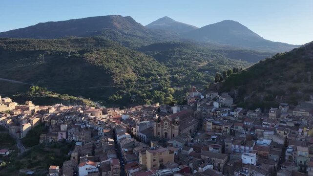 Aerial drone view of Collesano Sicilian mountain town at sunset with Basilica San Pietro church and historic stone streets in the Madonie Mountains, Sicily, Italy. Old mountain town in Sicily