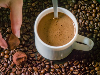Hand Taking a Chocolate Truffle Next to a Cup of Coffee