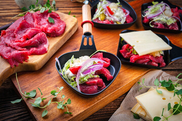 Traditional authentic swiss raclette with beef meat, pickles, Savoy cheese and spicy yogurt topping dip served as close-up on a wooden design board
