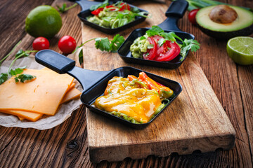Vegetarian raclette with mached avocado, lime and cheddar cheese served as close-up on awooden table
