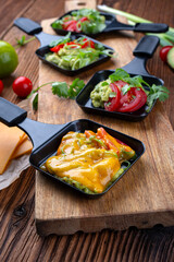 Vegetarian raclette with mached avocado, lime and cheddar cheese served as close-up on a wooden board