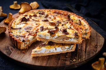 Authentic French tart with fresh chanterelles served as close-up on a wooden board