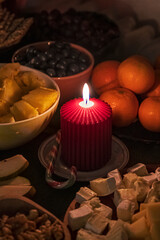 A warm holiday table scene with a lit red candle, mandarins, nuts and sweet. Cozy festive still life in Germany.