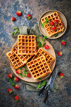 Fresh baked homemade Brussels waffles with ripe strawberries served as top vieew on a wooden plate