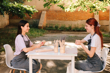 Clay art workshop outdoors. Two women enjoy a pottery class outdoors, shaping clay with smiles and creativity. 2 Girls sculpt clay in an outdoor workshop.