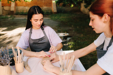 Clay art workshop outdoors. Two women enjoy a pottery class outdoors, shaping clay with smiles and creativity. 2 Girls sculpt clay in an outdoor workshop.