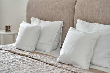 Elegant Bedroom Setting Featuring Plush White Cushions on a Soft Beige Headboard with a Cozy Blanket and a Decorative Candle for Relaxation