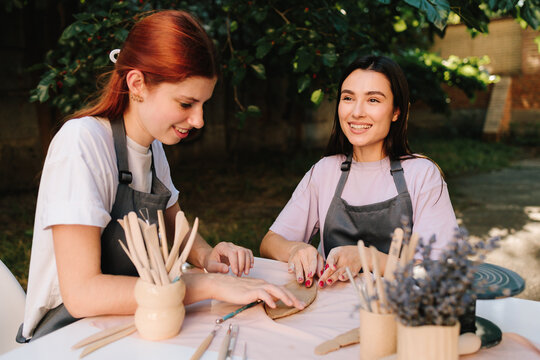 2 Girls sculpt clay in an outdoor workshop. Clay art workshop outdoors. Two women enjoy a pottery class outdoors, shaping clay with smiles and creativity. - Powered by Adobe
