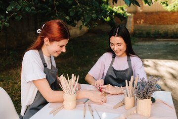 Clay art workshop outdoors. Two women enjoy a pottery class outdoors, shaping clay with smiles and creativity. 2 Girls sculpt clay in an outdoor workshop.