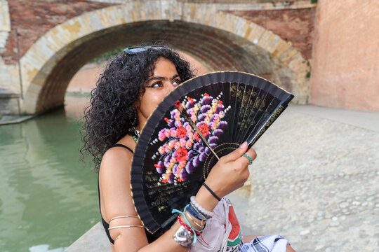 Woman Holding a Decorative Fan Near a Historic Bridge 