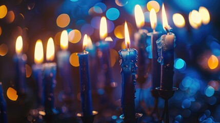 A close-up of lit Hanukkah candles with blue and gold bokeh in the background. The candles are various heights and colors, creating a warm, festive atmosphere