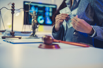 Person's hands holding cash and putting it into a blazer pocket, with Scales of Justice and gavel on a desk