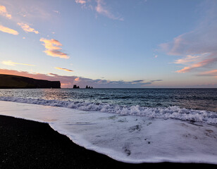 Sunset over black sand beach with ocean waves and sea stacks in Iceland
