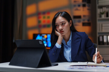 Fototapeta premium Businesswoman working late on a tablet at night, feeling tired and stressed in the office, experiencing burnout from overwork