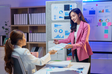 Young businesswomen working late, exchanging documents and analyzing financial charts and graphs during a corporate meeting