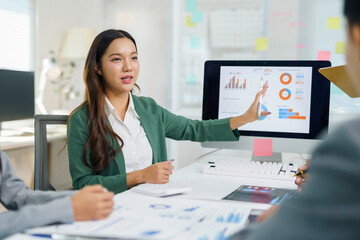 Businesswoman explaining financial data and market strategy to colleagues, discussing charts and graphs on computer screen