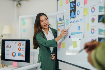 Business woman analyzing charts and graphs on a whiteboard, explaining strategy to colleagues during an office meeting