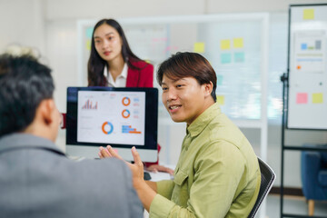 Asian business professionals discussing data charts on a computer screen, collaborating during an office meeting