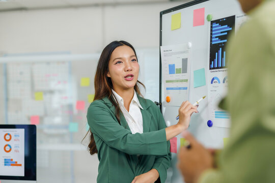 Young Asian businesswoman discussing financial data and charts on a whiteboard during a professional business meeting in an office setting