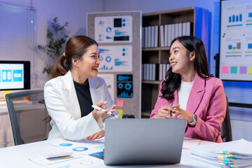Two smiling businesswomen intensely collaborating, analyzing data, and sharing ideas in a dynamic late night office work session
