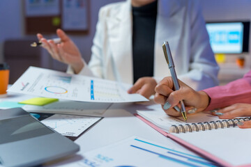 Business colleagues collaborating at an office desk, analyzing financial data reports and writing notes during a business meeting