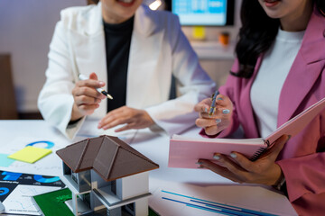 Businesswomen analyzing a house model and financial charts, planning a real estate project, collaborating on urban development