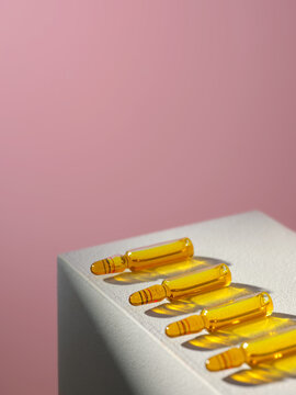 A row of yellow ampoules, resting on a white podium on pink background