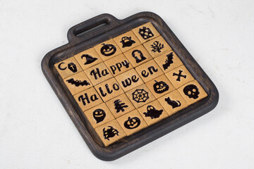 Halloween. Holiday Square cookies with black marmalade filling in the form of Halloween themed figures and words. On a wooden plate. White background. Close up