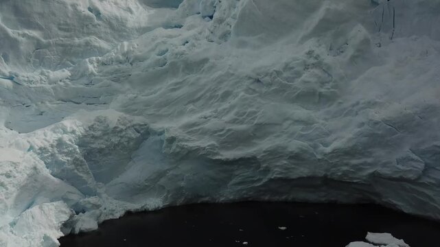 A snow-covered iceberg rises above cold, dark water. A panoramic view of the Antarctic winter landscape. Drone footage, a cinematic environmental scene.