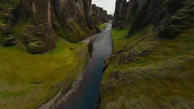 FPV drone diving down a step, moss-covered canyon clff.