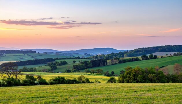 Panoramic vista showcases a tranquil landscape featuring rolling hills and lush green fields bathed in the soft light of a serene sunset, displaying a picturesque scene with vibrant colors.