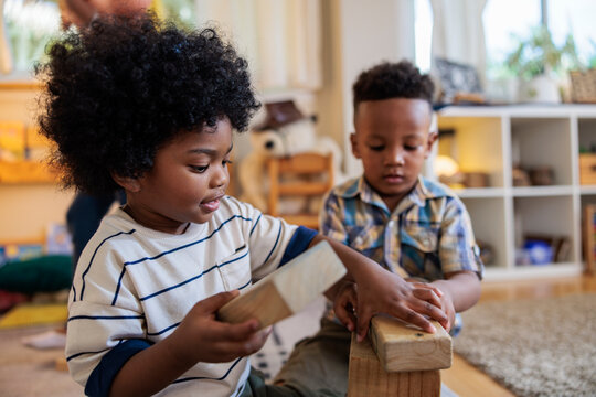 Two young boys play with wooden blocks indoors.
