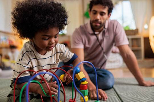 Child plays with bead maze, adult watches nearby.