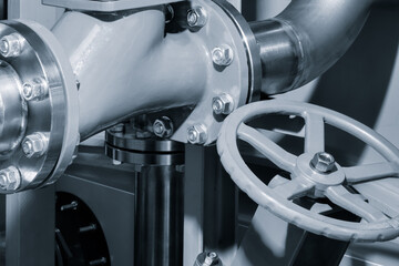 Silver pipe with a silver valve on it. The valve is closed. The pipe is connected to a larger pipe