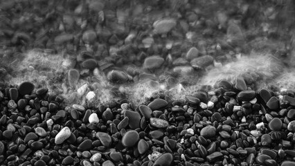 A beach with smooth pebbles and calm waves. The water is choppy, with waves crashing against the shore. Spa concept backdrop.