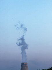 Industrial cooling tower releases plume into blue dusk sky, dramatic industrial landscape mood